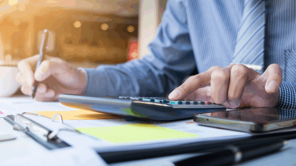 Person in business attire using a calculator and reviewing telecom billing software reports to track telecom expense optimization.